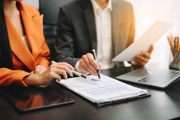 istock Business documents on office table with smart phone and calculator digital tablet and graph business with social network diagram and two colleagues discussing data working in the office 1516184801