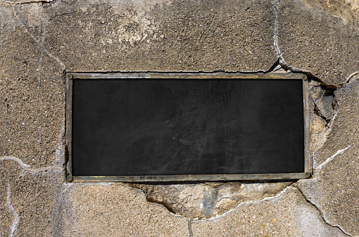 Old empty blackboard with metal rectangular frame with copy space on a cracked concrete wall. Photography.