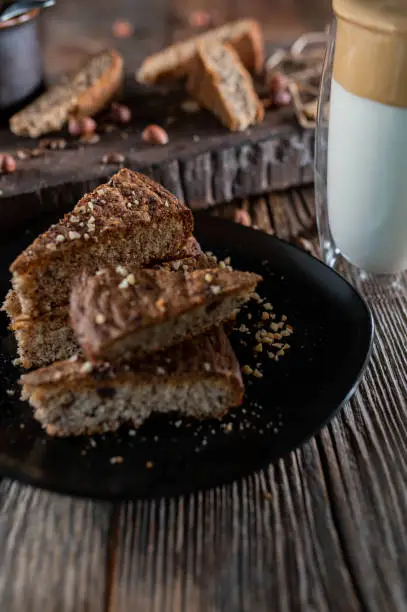 Delicious homemade hazelnut cake with dark chocolate. Served sliced on a black plate on rustic and wooden background with a glass of dalgona coffee.
