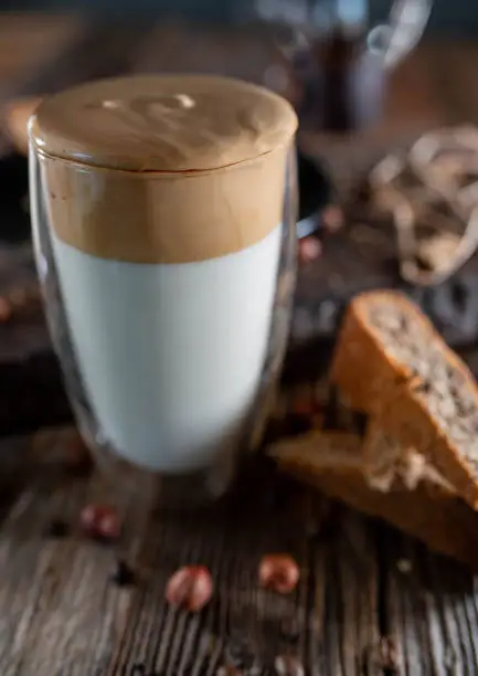 Fresh dalgona coffee in a thermo glass with homemade nut cake on wooden table background. Closeup, front view