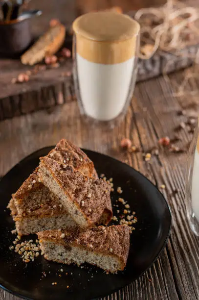 Fresh baked hazelnut cake served sliced on a platter with dalgona coffe on rustic and wooden table background with decoration from above.