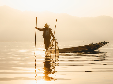 Lake Inle, Myanmar - March 03, 2010:  Fisherman trying to catch fish during early morning at famous Inle lake of Myanmar in his wooden boat.