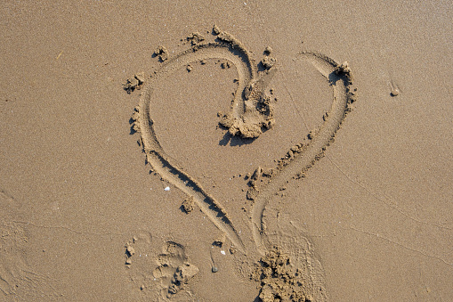 Drawing heart shape love concept on sand at the beach with vacation holiday summer travel background. Heart shape and footprint on wet sand.