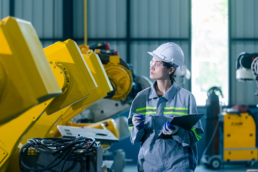 Female engineers working robot assembly industry plant in factory holding clipboard checking inspection quality robotic arm. Woman technician robotic industrial.