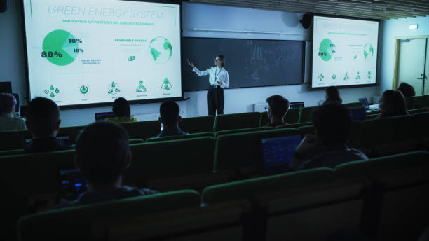 istock Young Postgraduate PhD Student Giving a Renewable Energy Lecture to Diverse Multiethnic Group of Women and Male Scholars in Dark College Room. Projecting Slideshow with Different Types of Green Energy 1516259249