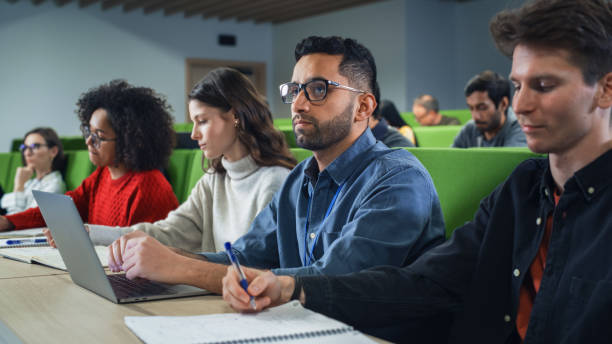istock Smart Handsome Male Student Studying in University with Diverse Multiethnic Classmates. Young Man is Using a Laptop Computer to Summarize the Lecture, Study at Home and Pass the Exams 1516269031