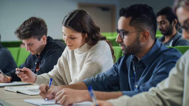 istock Talented Smart Female Student Studying in College with Diverse Multicultural Colleagues. Young Woman Focused on a Lecture, Writing Down a Summary in Her Notebook 1516271786