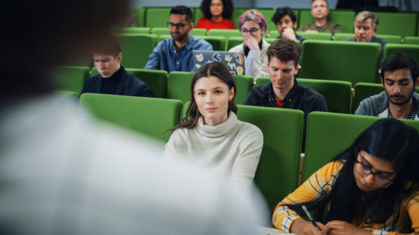 istock Diverse Multicultural Students Studying in University Room, Listening to a Professor Giving a Lecture. Smart Enthusiastic Young Adults Sitting in Classroom. Over the Shoulder Photo 1516273883
