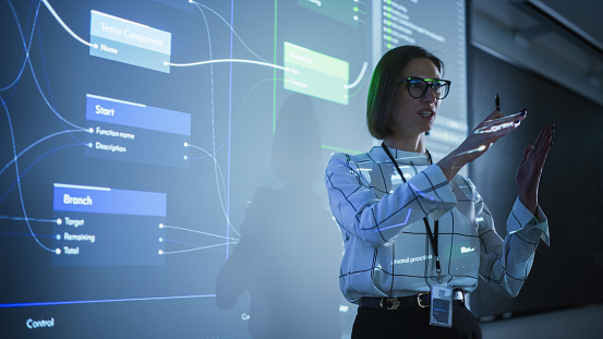 Young Businesswoman Presenting a Web Development Road-Map in a Dark Room with Projecting Images. Female University Professor Showing Initial Steps to a Successful Project Completion