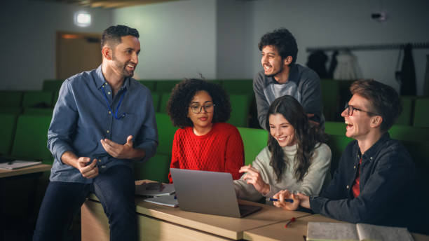 istock Diverse Happy Students Having a Conversation with a Teacher in University Classroom, Working on a Shared Research Project on a Laptop Computer. Classmates Working Together on College Science Project 1516283133