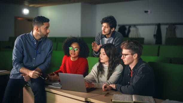 istock Group of Diverse Happy Students Having a Conversation in University Classroom, Working on a Shared Research Project on a Laptop Computer. Classmates Working Together on College Homework 1516283148