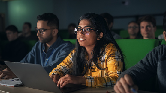 Portrait of a Smart Talented Indian Female Student Studying in University with Diverse Multiethnic Classmates. Young Woman Using Laptop Computer and Taking Notes During the Lecture