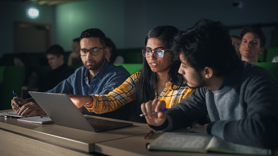 Group of Multiethnic Enthusiastic Students Collaborate in University Classroom, Compare Research Project Findings on a Laptop Computer. Diverse Scholars Working as a Team on College Homework