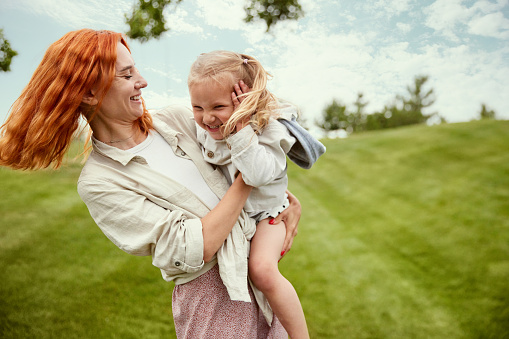 Happiness. Beautiful redhead young woman, mother playing with her little daughter in the park on warm summer day. Concept of family, childhood and parenthood, fun, weekends, love, ad