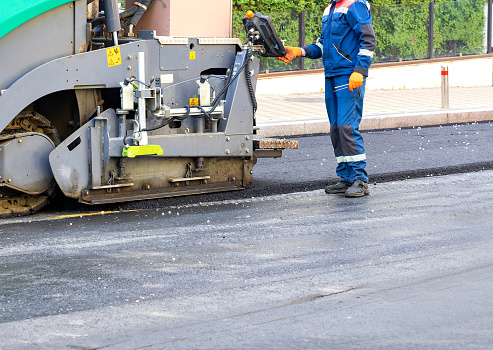 A fragment of the process of the work of an asphalt paver under the control of an operator engineer on a town road on a summer day. Copy space.