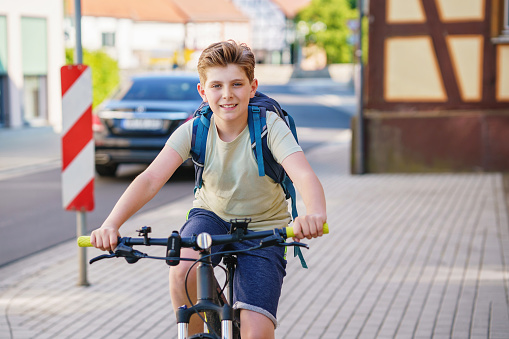 Handsome preteen boy going to school on bike. Teenager ride bicycle. Safe way to high school. Happy child boy with backpack on bike. Healthy outdoor activity for young student
