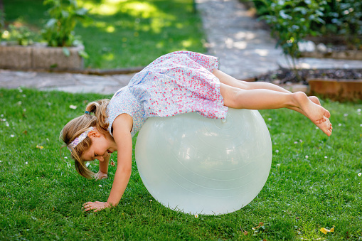 Little cute girl doing exercises with ball outdoors. Active preschool child having fun with sports. Outdoor children activity in summer