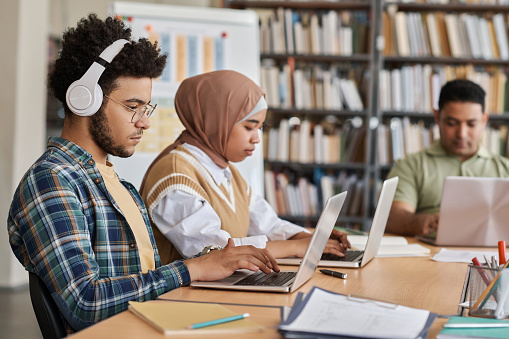 Group of foreign students using computers in their study while sitting at table in the library