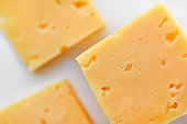 Yellow pieces of cheese on a white background. Square cheese. Delicious cheese snack.