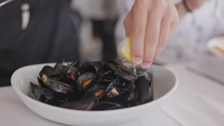 Closeup of a boy squeezing lemon over bowl of mussels