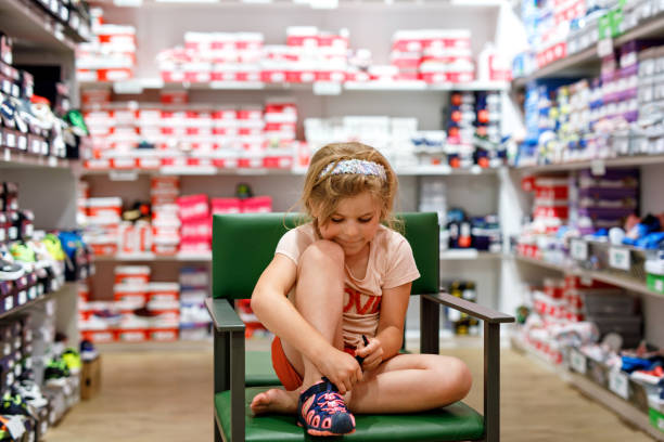 행복한 어린 소녀는 상점에서 새 신발을 신중하게 선택하고 구입하여 완벽한 신발을 찾기 위해 다양한 옵션을 시도합니다. 흥분한 미취학 아동. 스톡 사진