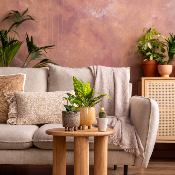 istock Stylish composition of creative spacious living room interior with plants, sofa, coffee table, rattan chest of drawers and stylish accessories. Botanical space of a cozy room. Brown walls. Template. 1516405568