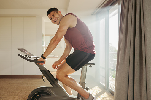 Young man enjoys smashing his goals in his indoor cycling workout. Athlete using his high-tech training equipment to get the most out of his home gym and push himself to new heights of fitness.