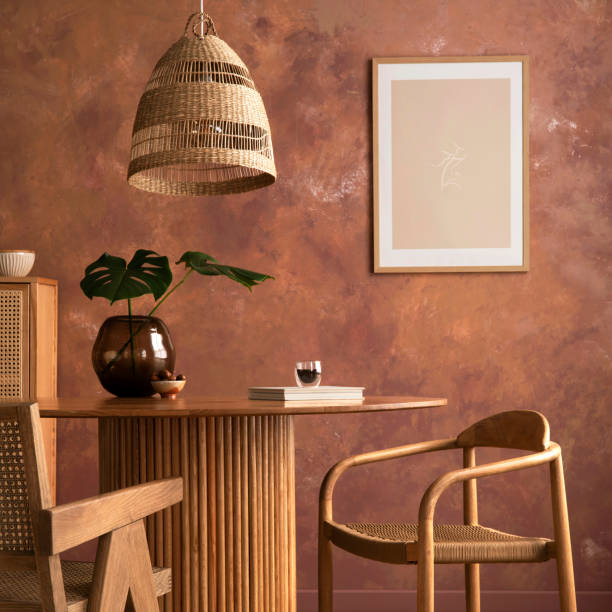istock Stylish boho vintage dining room interior with poster mock up. Round table with rattan armchair, vase with dried flowers and cup. Brown wall and rattan lamp. Mock up poster. Template. 1516472347