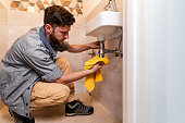 A plumber holds a rag over a siphon leak under a bathroom sink