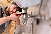 A plumber carefully fixes a leak in a sink using a wrench