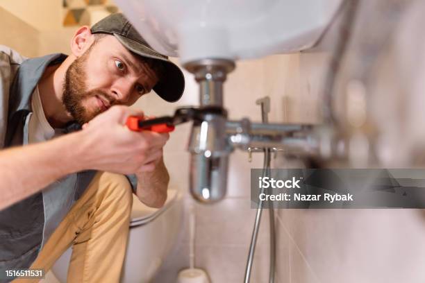 A Plumber Carefully Fixes A Leak In A Sink Using A Wrench Stock Photo - Download Image Now