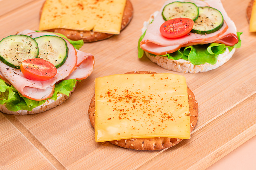 Light Breakfast. Quick and Healthy Sandwiches. Rice Cakes with Ham, Tomato, Fresh Cucumber, Green Salad and Cheese on Wooden Cutting Board. Beige Background
