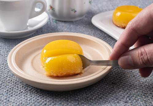 Hand holding fork cutting quindim, traditional egg and coconut brazilian dessert.