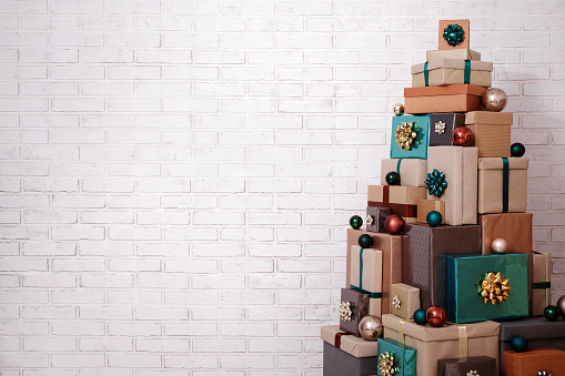 Christmas background - wrapped gift boxes laid out in the shape of a Christmas tree and copy space over white brick wall