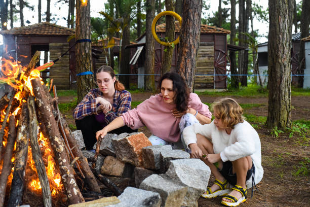 Mother with her daughters spending time together, kindle a fire and throw sticks