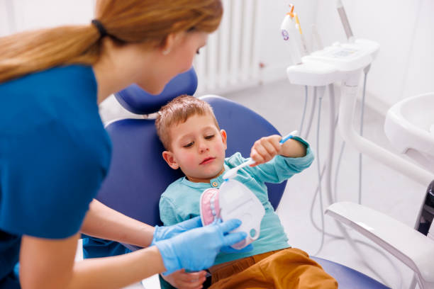 Female dentist demonstrating proper tooth brushing technique to child patient stock photo