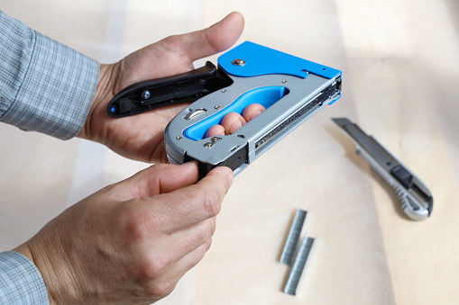 Hands open construction stapler to fill it with new staples for job, close-up