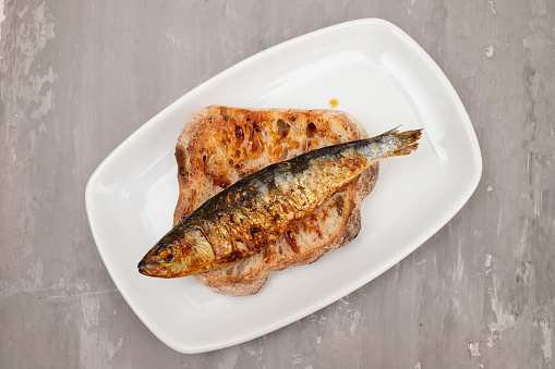 Grilled sardines with sauce on fresh bread on white dish