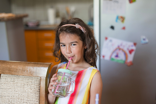 Cheerful beautiful girl drinking water from a jar with a straw