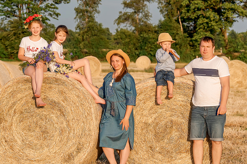 Happy large family on a summer field against the backdrop of haystacks. A beautiful family is sitting on a haystack
