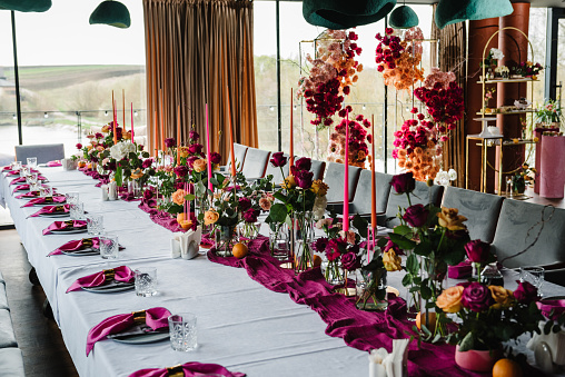 Beautifully organized event, served table banquet ready for guests in hall. Table set for a birthday party or wedding reception. Decoration with pink and orange flowers roses and candles and fruits.