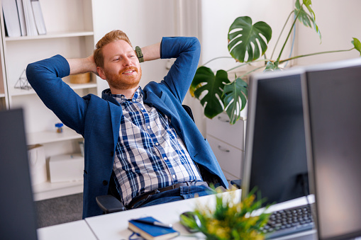 Confident successful businessman sitting at his desk taking a break and relaxing while working in an office, smiling and stretching out