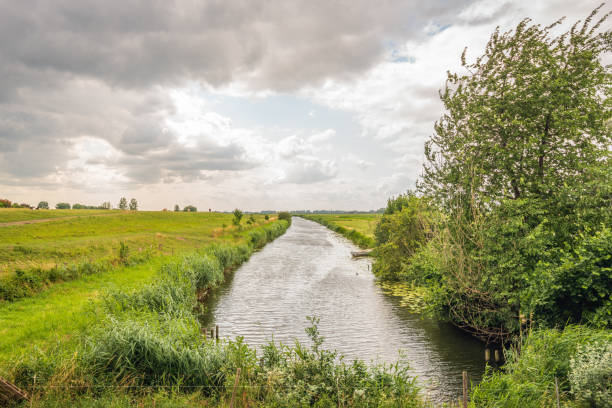 Picturesque polder landscape with perspective on a cloudy and stormy day in the spring season. A rowing boat is moored on one of the banks. The photo was taken in the Dutch province of North Brabant.
