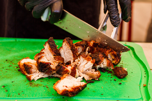 A man is chopping with an knife, wearing gloves, a well-seasoned barbecue roast pork with crackling. Tender, juicy and bursting with smoky deliciousness.