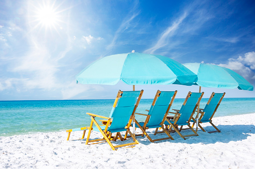 A group of blue beach chairs with umbrellas sitting on white sandy beaches in front of the ocean on a sunny day.