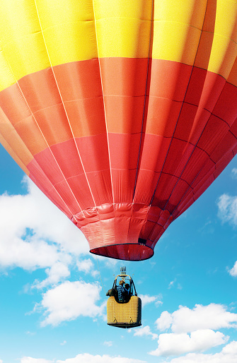 A vintage film photograph of a red and yellow hot air balloon against a blue cloudy sky.