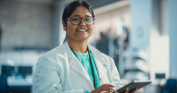 istock Portrait of Indian Young Female Scientist Using Digital Tablet Computer, Looking at Camera and Smiling in a Laboratory. Confident Professional Woman Working as Engineer, Monitoring Technology Projects 1516696891