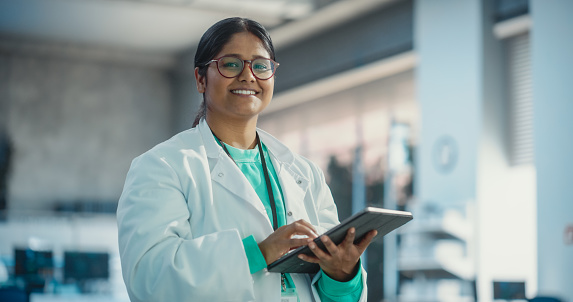 Portrait of Young Indian Female Specialist in a Lab Coat Smiling and Using Laptop Computer. Professional and Successful Woman Working as an Engineer, Thinking and Developing High Tech Projects
