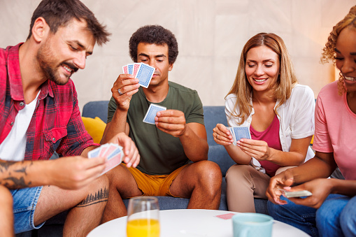 Group of cheerful young friends spending leisure time together at home, having fun playing card games