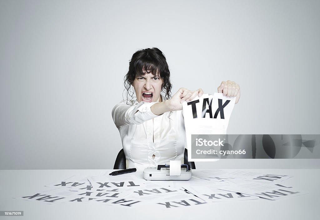 No tax! Young desperate woman at her paperwork-covered desk ripping up a tax form staring at the camera Humor Stock Photo
